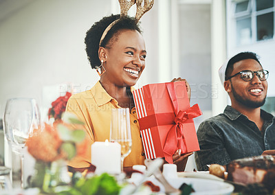 Buy stock photo Cropped shot of an attractive young woman smiling while holding a present during Christmas lunch at home