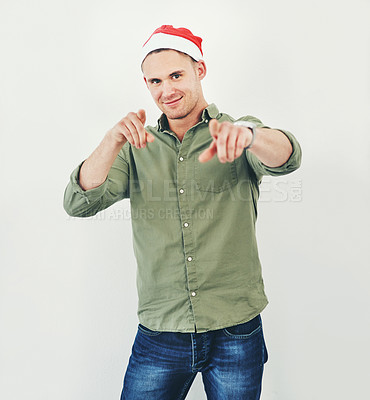 Buy stock photo Christmas, portrait and festive with a model man in studio on a gray background wearing a hat for the holidays. Tradition, celebration and seasons greetings with a male in a santa cap while pointing