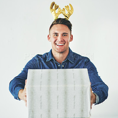 Buy stock photo Christmas, present and celebration with a festive man in studio on a gray background in the holiday season. Tradition, gift and giving with a cheerful male wearing reindeer horns on his head