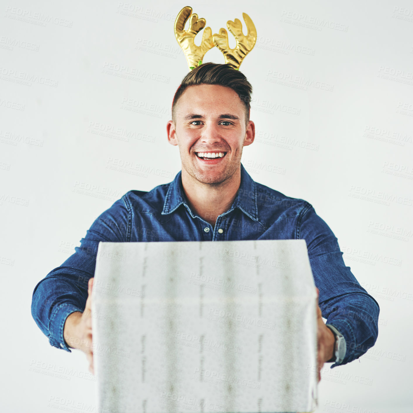 Buy stock photo Christmas, present and celebration with a festive man in studio on a gray background in the holiday season. Tradition, gift and giving with a cheerful male wearing reindeer horns on his head