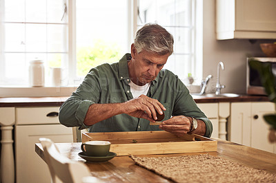 Buy stock photo Cropped shot of a relaxed senior man preparing to roll a marijuana joint to smoke inside the kitchen at home during the day