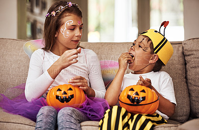 Buy stock photo Cropped shot of a young brother and sister eating their Halloween candy while sitting on their sofa at home