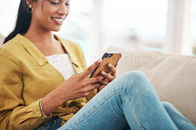 Buy stock photo Cropped shot of an attractive young businesswoman sitting on her couch and using her cellphone while at home
