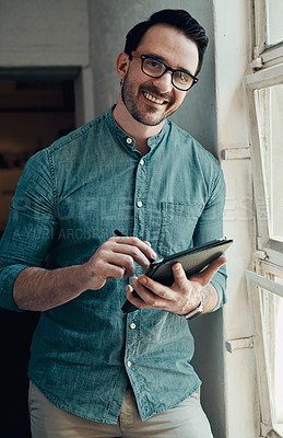 Buy stock photo Cropped portrait of a handsome young businessman smiling while using a digital tablet  in a modern office