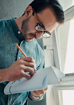 Buy stock photo Cropped shot of a handsome young male architect writing on a blueprint while standing in a modern office
