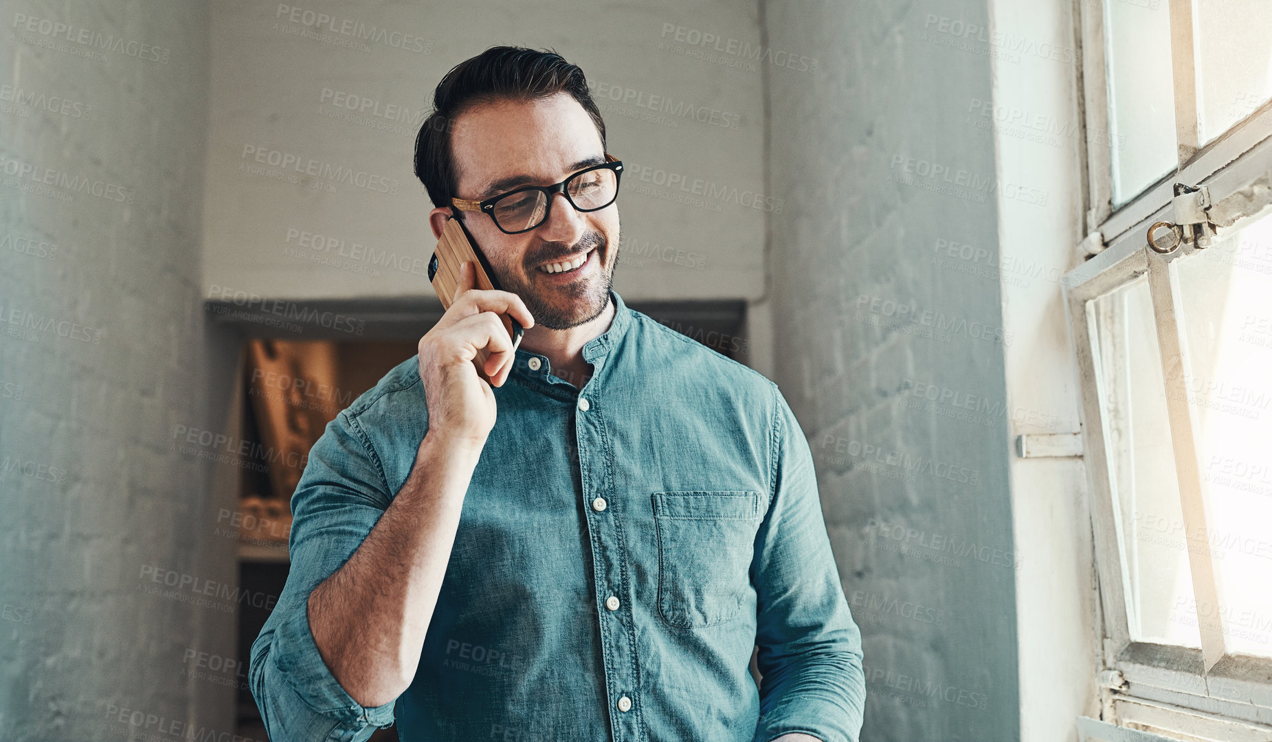Buy stock photo Cropped shot of a handsome young male architect taking a phonecall while standing in an office