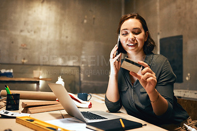 Buy stock photo Cropped shot of an attractive young female carpenter holding her credit card and doing online shopping while talking on her cellphone inside of a workshop