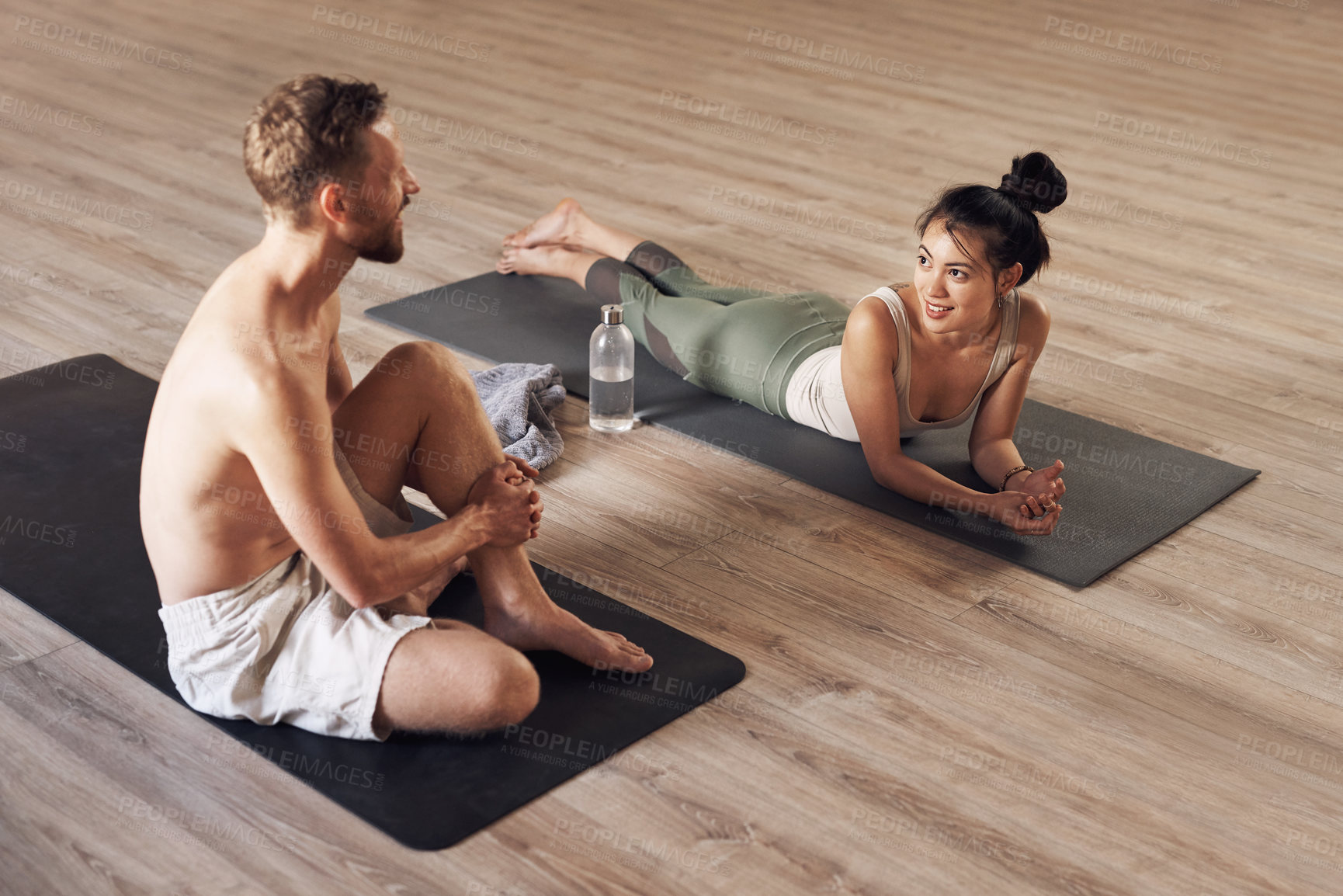 Buy stock photo Full length shot of two young people taking a break and chatting while working out together inside a yoga studio