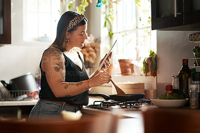 Buy stock photo Shot of a young woman using a digital tablet while preparing a meal at home