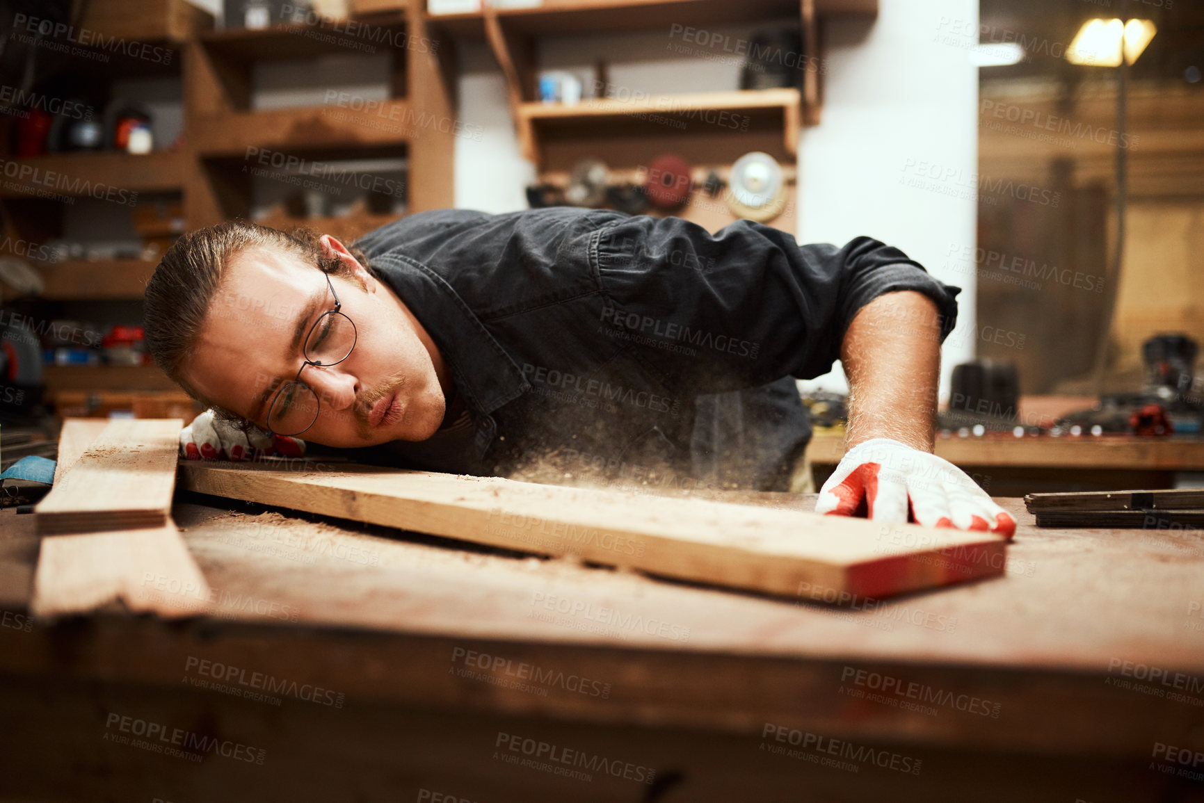 Buy stock photo Man, carpenter or blowing dust with wood on workbench for project or woodwork at manufacture. Young, male person or designer with material, tools or equipment for DIY, artisan or crafting at workshop