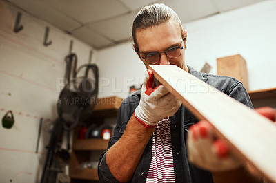 Buy stock photo Cropped shot of a focused young male carpenter looking down the surface of a piece of wood that he sanded down inside of his workshop