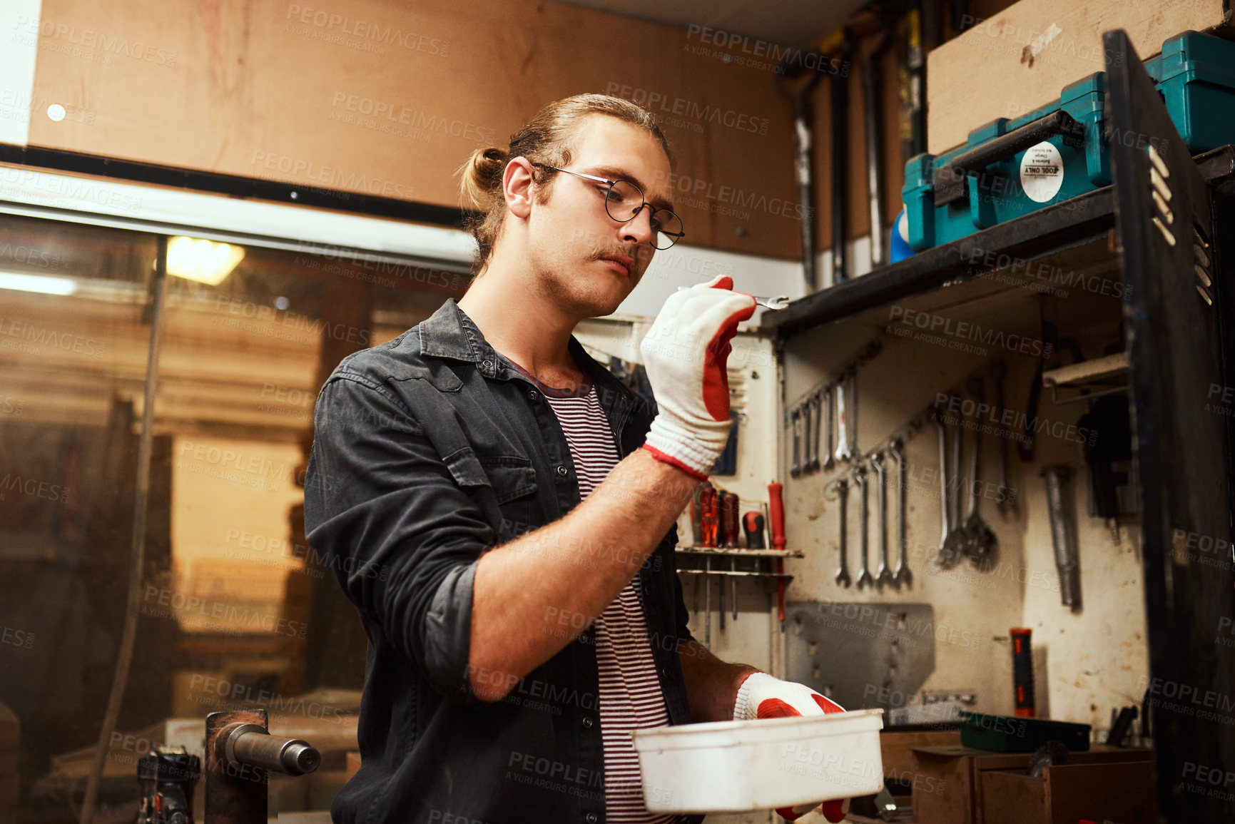Buy stock photo Cropped shot of a focused young male carpenter holding a small spanner in his  hands to use inside of his workshop at night