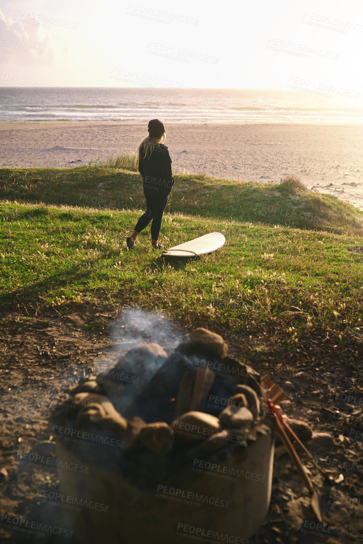 Buy stock photo Woman, beach and relax with surfboard by camp fire for adventure, break and holiday in Australia. Female person, seaside and standing for hobby or sports with training, exercise or workout to explore