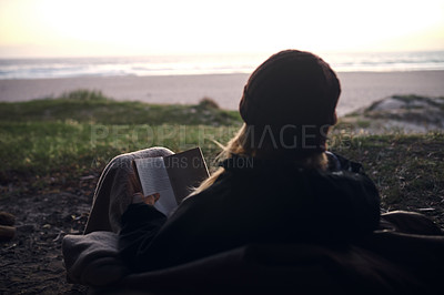 Buy stock photo Rearview shot of a young woman reading a book outdoors