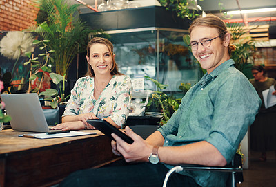 Buy stock photo Cropped portrait of two young businesspeople sitting and working on technology during a discussion in their floristry