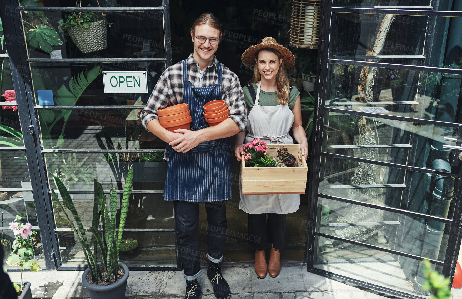 Buy stock photo Full length portrait of two young business owners standing at the entrance of their floristry together and holding potting supplies