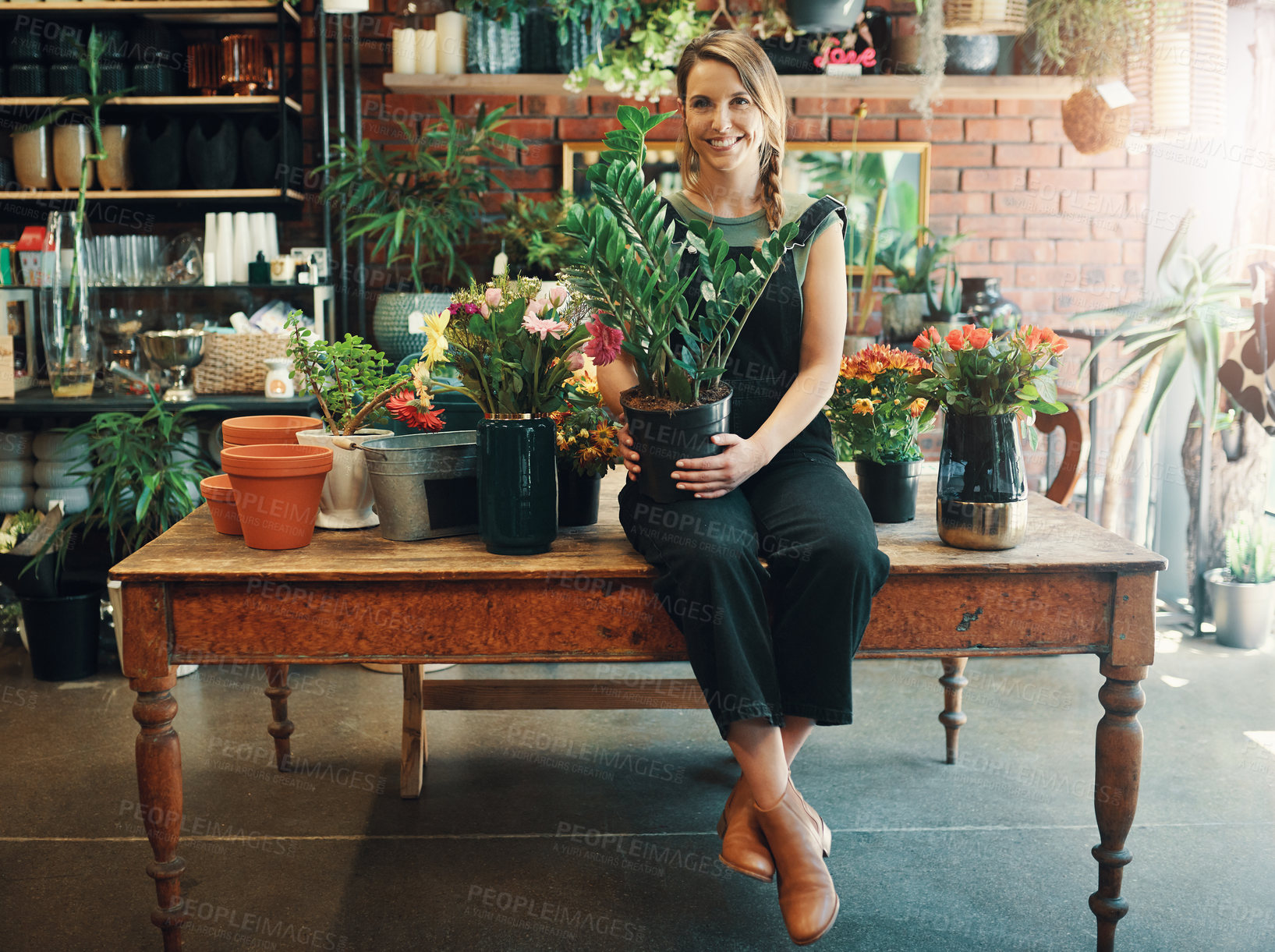 Buy stock photo Full length portrait of an attractive young business owner sitting alone in her floristry and holding a pot plant