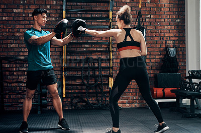 Buy stock photo Cropped shot of an attractive young female boxer working out with her personal trainer in a gym