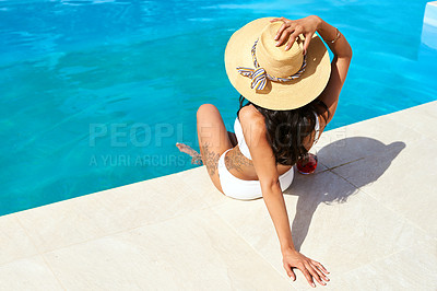 Buy stock photo Rearview shot of a young woman relaxing by the pool on a sunny day