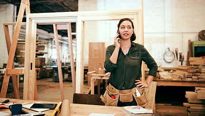 Buy stock photo Shot of a female carpenter talking on her cellphone while standing in her workshop