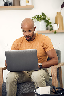 Buy stock photo Shot of a young man using his laptop while sitting on the sofa at home