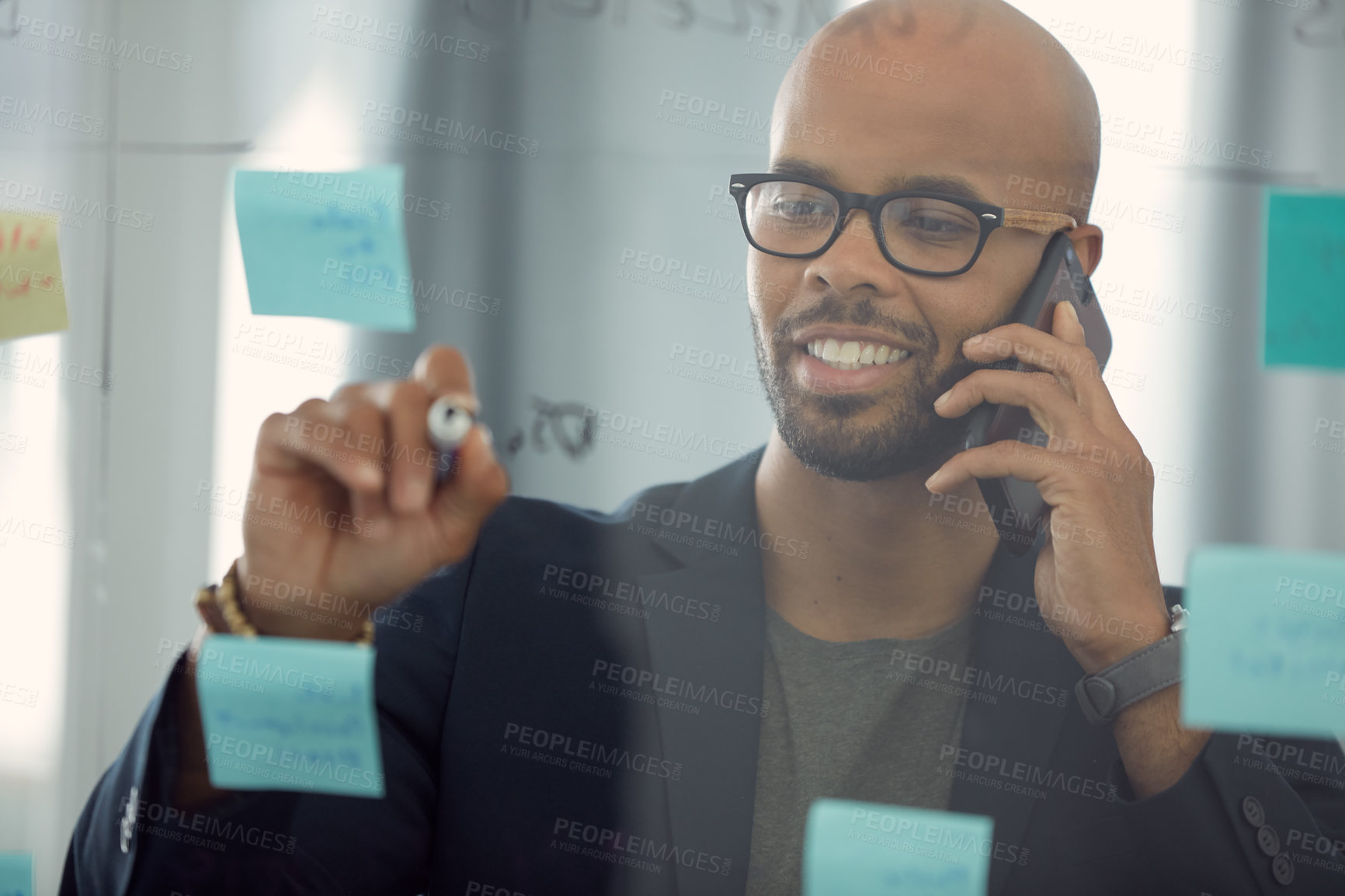 Buy stock photo Shot of a young businessman talking on the phone while brainstorming on a glass wall