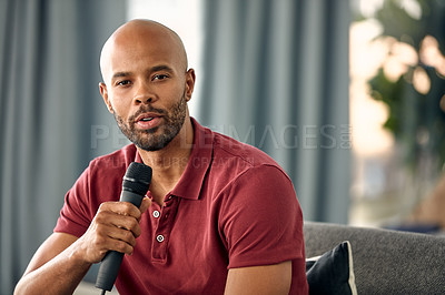 Buy stock photo Cropped shot of a young man sitting on a sofa while speaking over a microphone