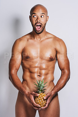 Buy stock photo Portrait of a naked man posing with a pineapple covering his genital area against a grey background