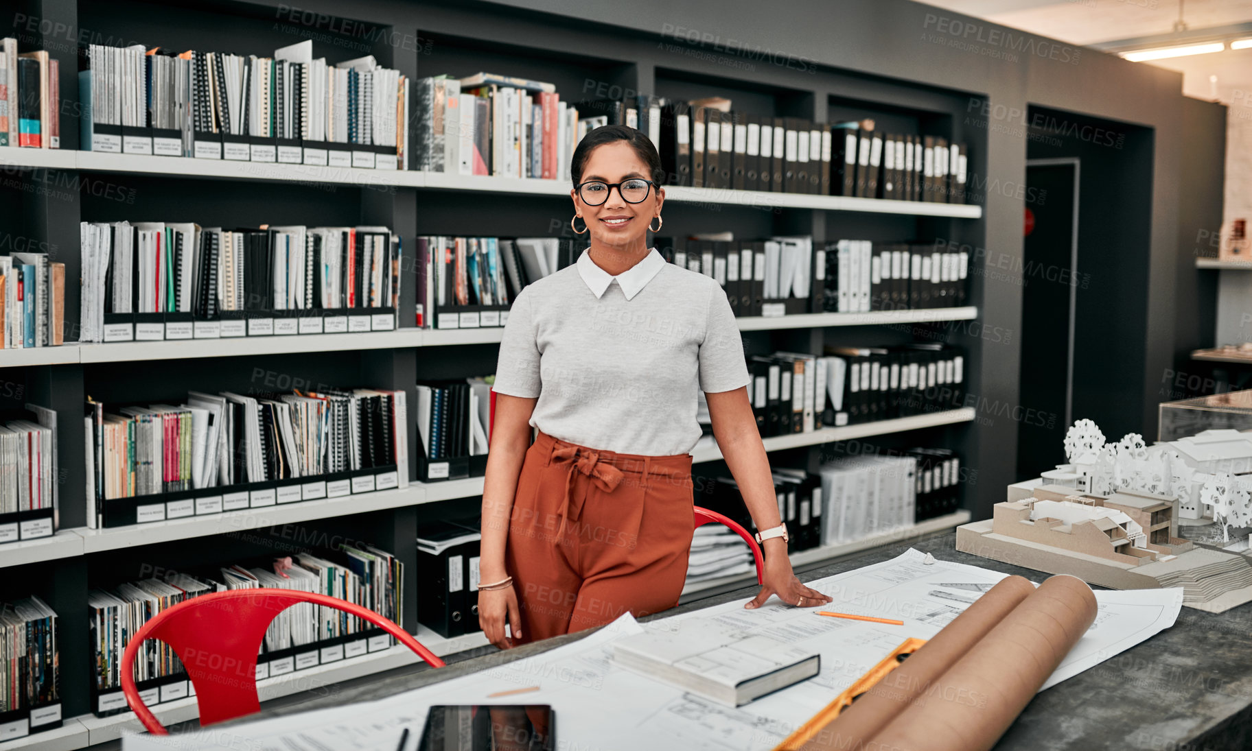 Buy stock photo Cropped portrait of an attractive young female architect smiling while working with blueprints in her office