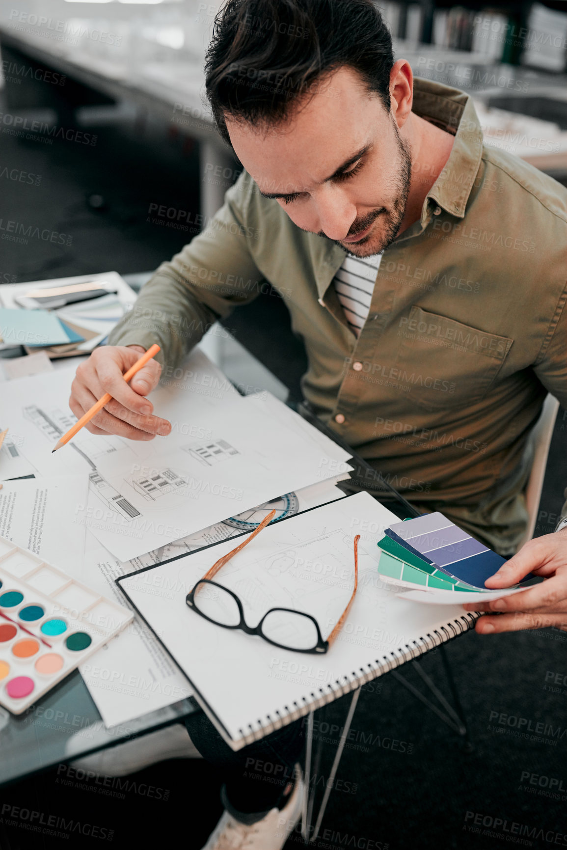 Buy stock photo Cropped shot of a handsome young male architect working with some blueprints in a modern office