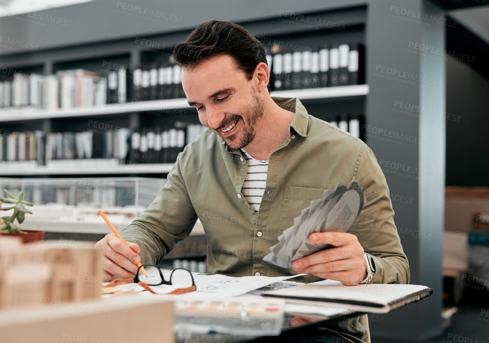 Buy stock photo Cropped shot of a handsome young male architect smiling while working with some blueprints in a modern office