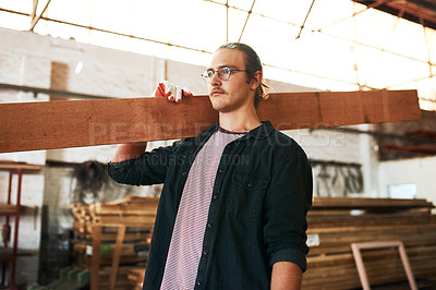 Buy stock photo Shot of a handsome young carpenter carrying a wooden plank over his shoulders inside a workshop