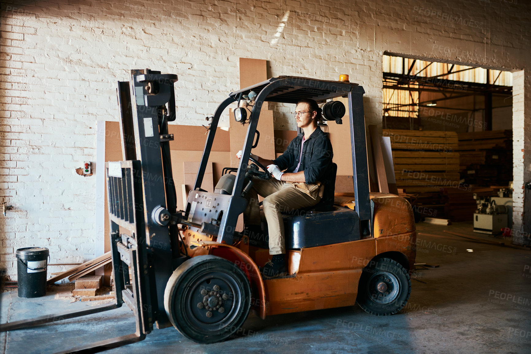 Buy stock photo Shot of a young male warehouse worker driving a forklift
