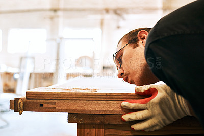 Buy stock photo Shot of a handsome young carpenter blowing dust off a wooden plank inside a workshop