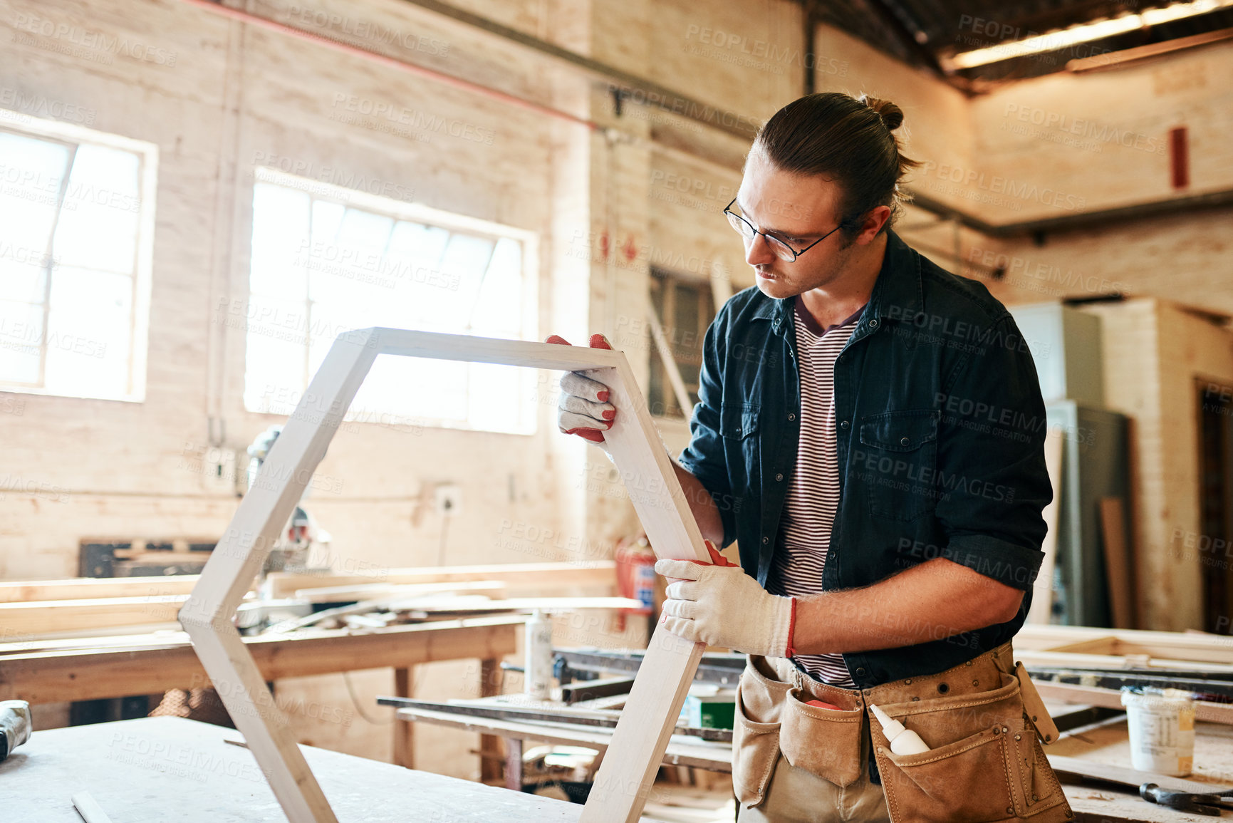 Buy stock photo Shot of a handsome young carpenter working on a wooden frame inside a workshop