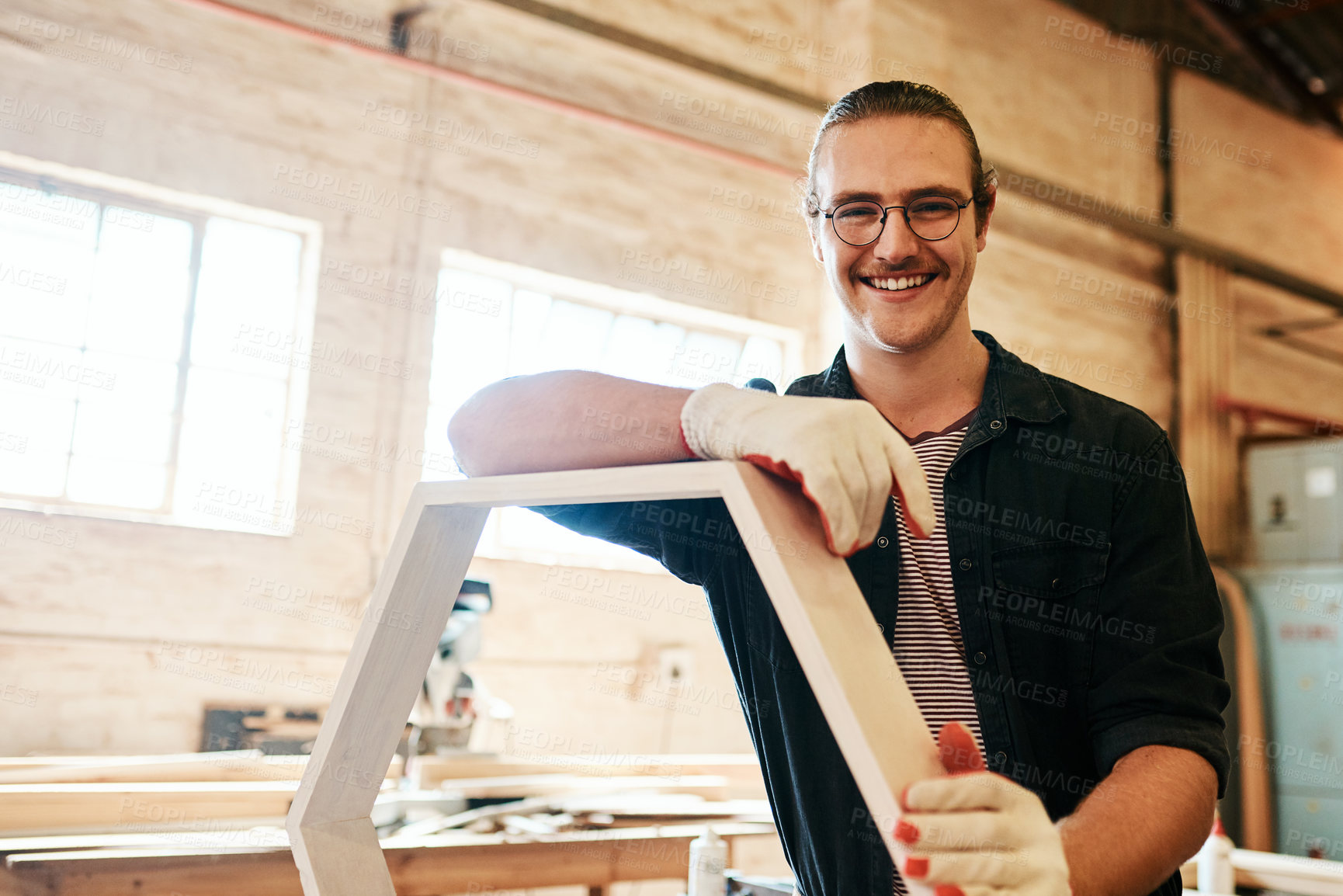 Buy stock photo Portrait of a handsome young carpenter working on a wooden frame inside a workshop