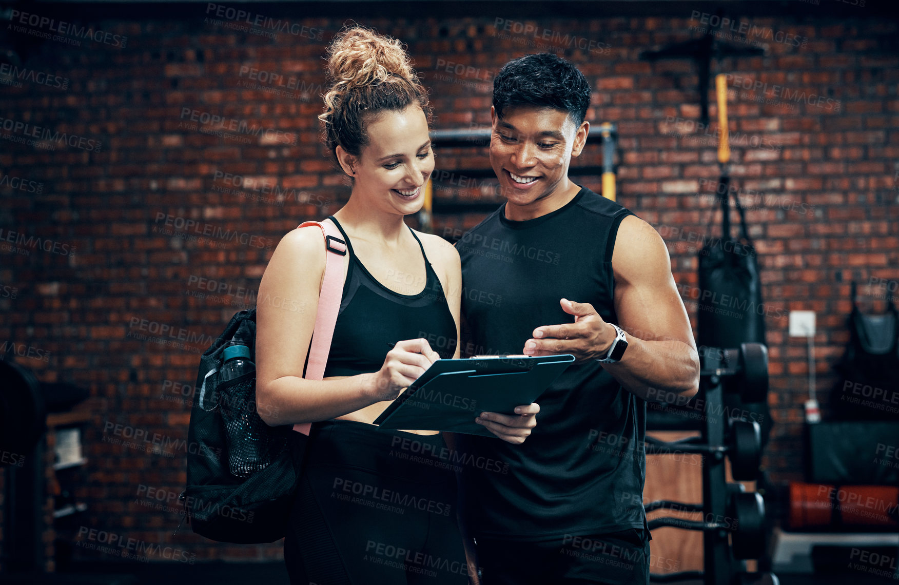 Buy stock photo Shot of a sporty young woman talking to a fitness trainer at the gym