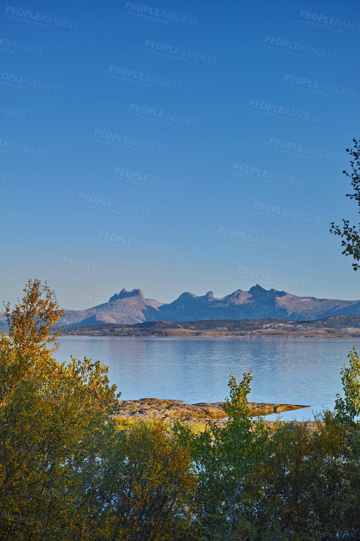 Buy stock photo A sea landscape near a mountain with a blue sky background and copy space. Vibrant outdoors by the ocean or beach with lush green plants or nature hills and copyspace on a summer day