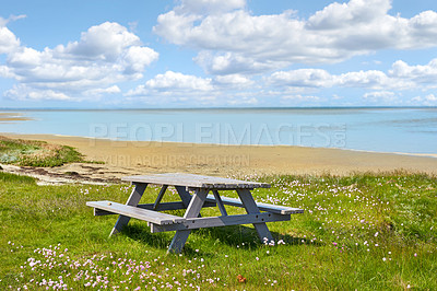 Buy stock photo Wooden picnic bench and table at the sea with cloudy blue sky background outdoors. Seating furniture at the beach to enjoy a peaceful day at the coast while taking a break from travel and exploring
