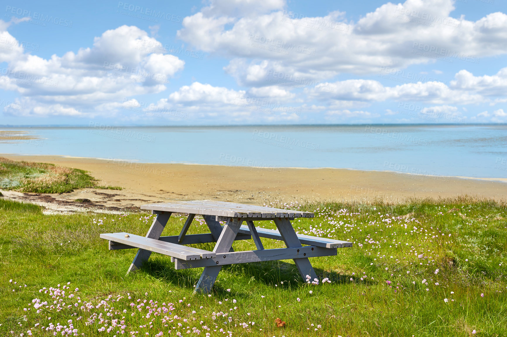 Buy stock photo Wooden picnic bench and table at the sea with cloudy blue sky background outdoors. Seating furniture at the beach to enjoy a peaceful day at the coast while taking a break from travel and exploring