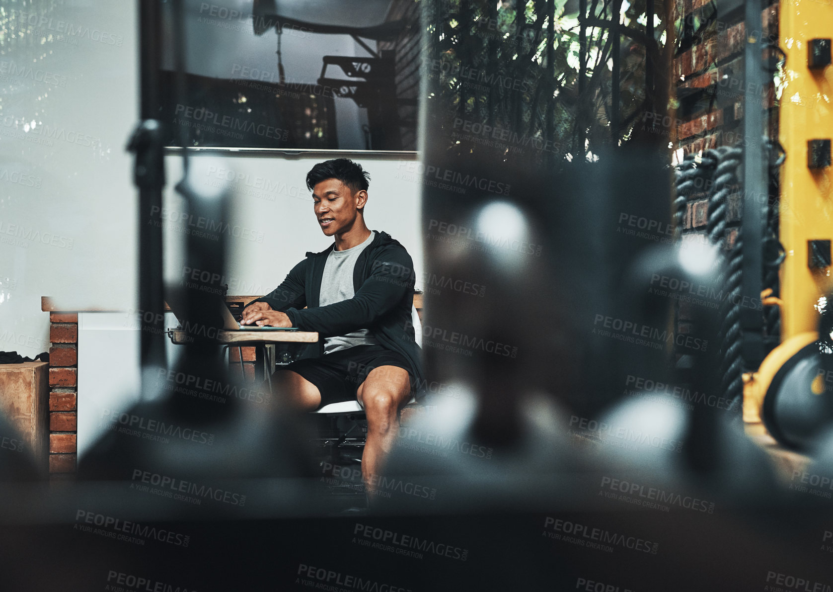 Buy stock photo Cropped shot of a handsome young male fitness instructor using a laptop while working in a gym