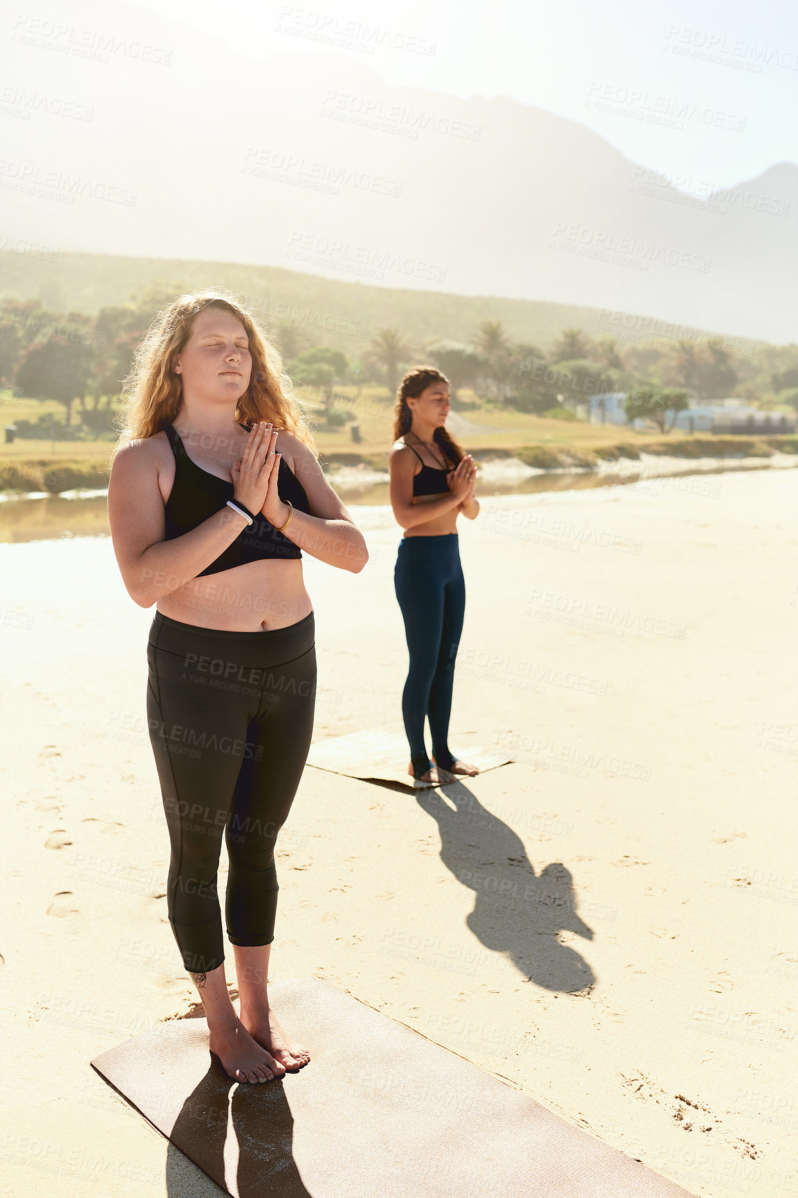 Buy stock photo Shot of two young women practising yoga on the beach