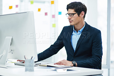 Buy stock photo Shot of a young businessman working on a computer in an office