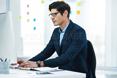 Buy stock photo Shot of a young businessman working on a computer in an office