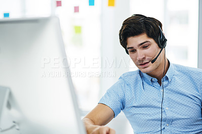 Buy stock photo Shot of a young businessman using a headset while working on a computer in an office