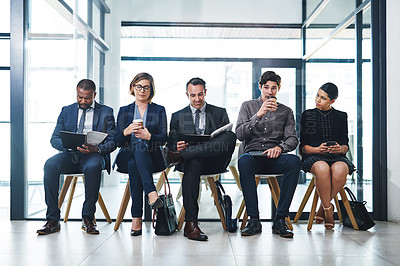 Buy stock photo Full length shot of a diverse group of businesspeople sitting in line for an interview in a modern office