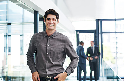 Buy stock photo Cropped portrait of a handsome young businessman smiling in a modern office with his colleagues in the background