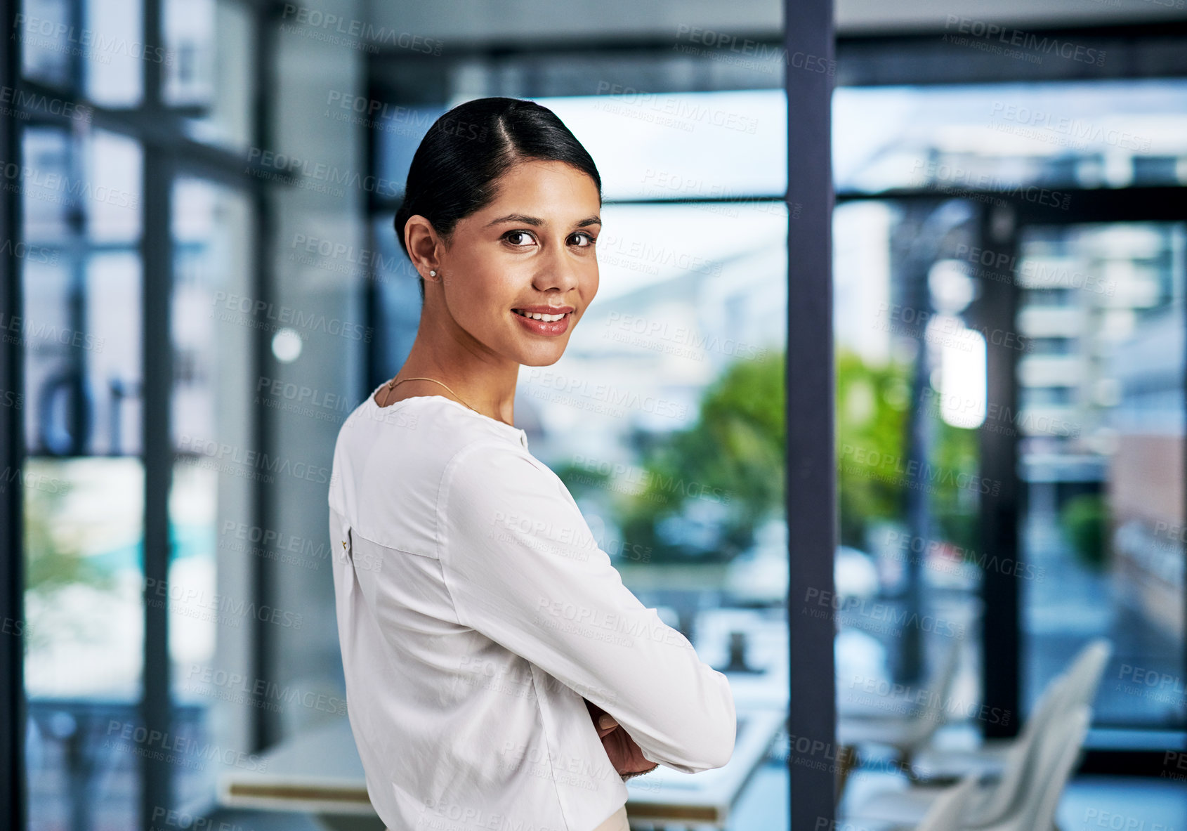 Buy stock photo Cropped portrait of an attractive young businesswoman smiling while standing with her arms folded in a modern office