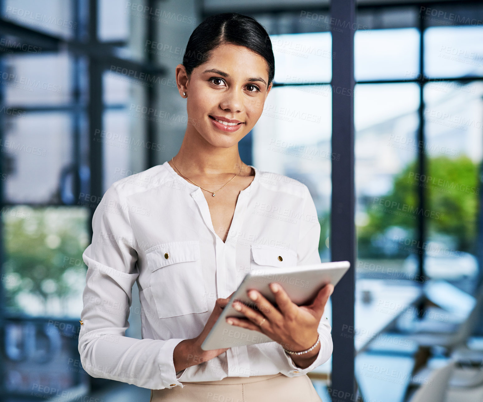 Buy stock photo Cropped portrait of an attractive young businesswoman smiling while using a digital tablet while standing in a modern office