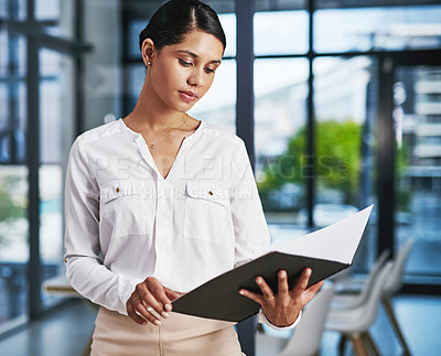 Buy stock photo Cropped shot of an attractive young businesswoman reading a file while standing in a modern office